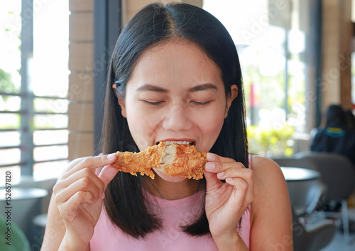 Close up of young asian woman eating fried chicken in cafe.