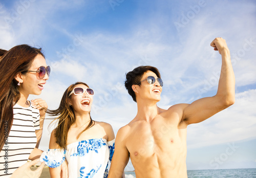 young man showing her friends his big muscles on beach.