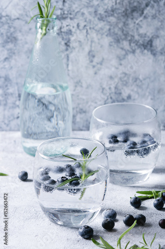 Tonic water cocktail with rosemary and blueberries. Two cold glasses and bottle with bubbles over gray blue texture background. Refreshing beverage alco non alcohol