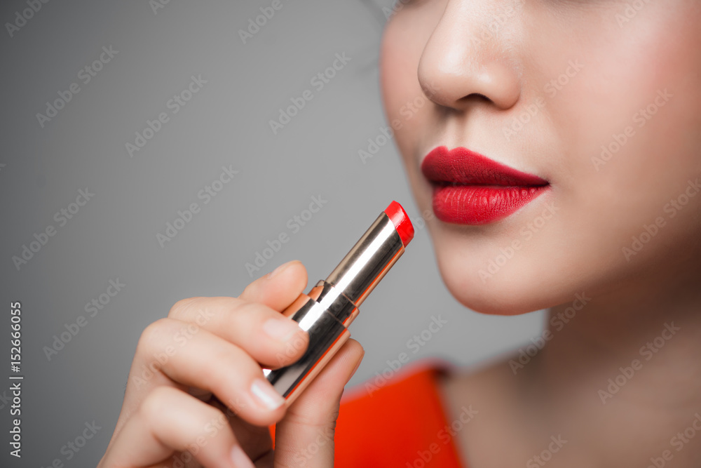 Close up portrait of attractive girl holding red lipstick over grey background Close up portrait of attractive girl holding red lipstick over grey background