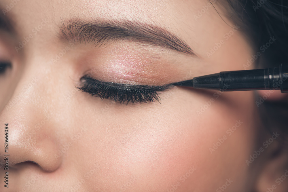 Close-up portrait of beautiful girl touching black eyeliner to her eyelid with closed eyes.