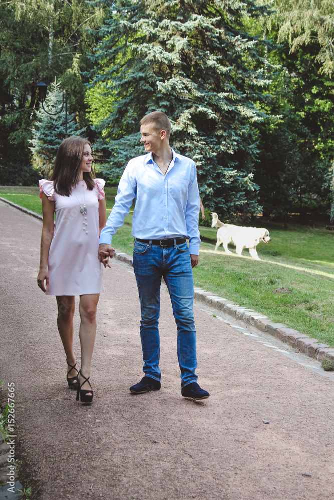 Couple holding hands while walking in park. Girl dressed in pink dress and man in blue shirt and jeans. Couple holding hands while walking in park. Girl dressed in pink dress and man in blue shirt and jeans.