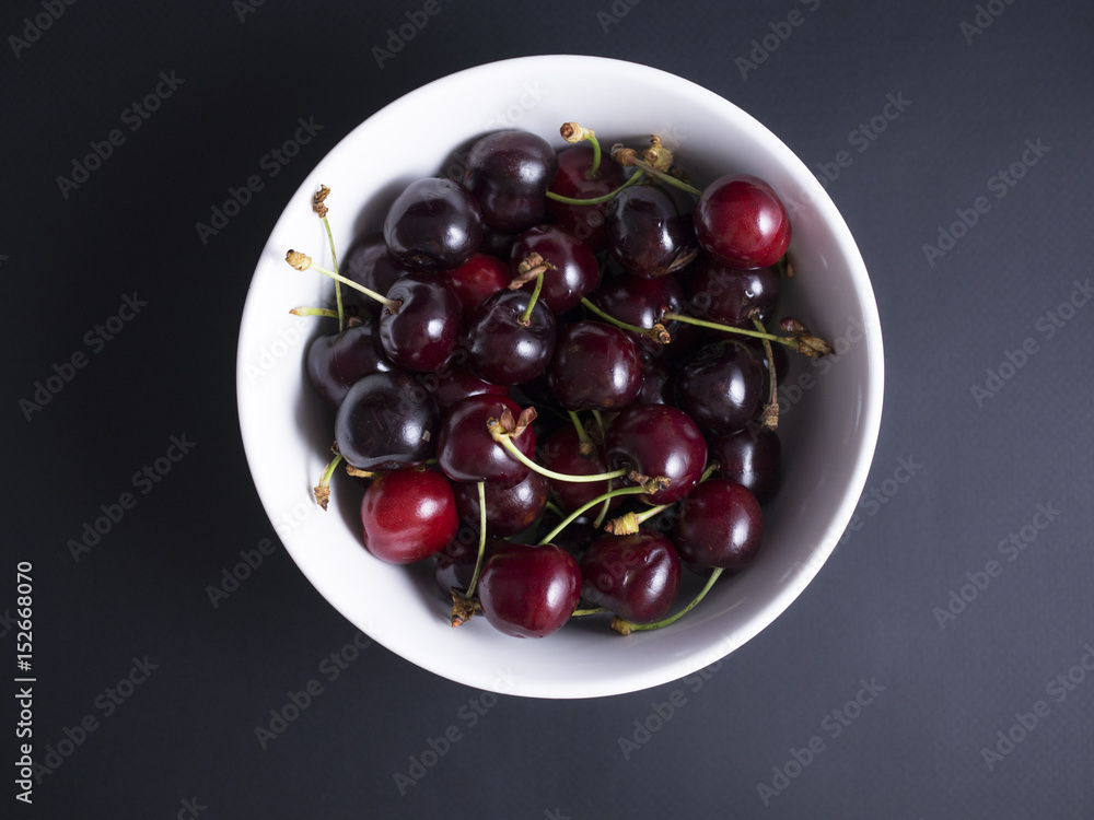 Fresh ripe red and black cherries in a white bowl isolated on black background Fresh ripe red and black cherries in a white bowl isolated on black background