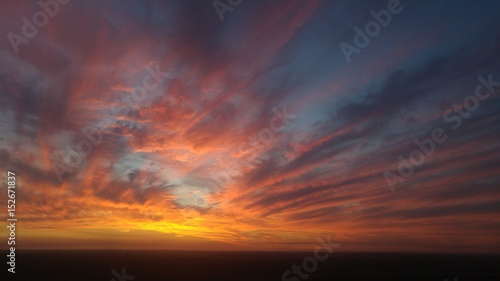 Sky on fire lighting up the clouds a myriad of colors at sunset on open farmlands. © mat_millard