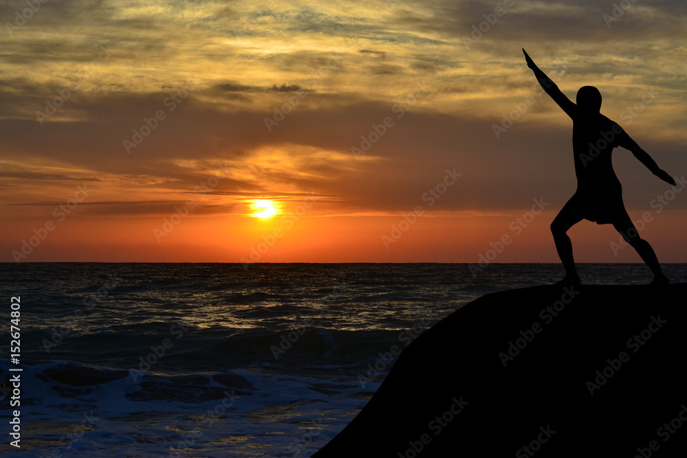 Man silhouette in a yoga pose on the shore at sunrise
