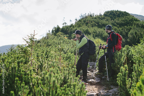 Two hikers with backpacks are trekking in green mountains