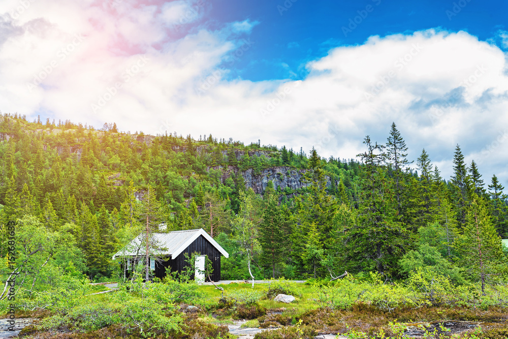 Traditional norwegian wooden house standing at the lakeside and mountains in the distance