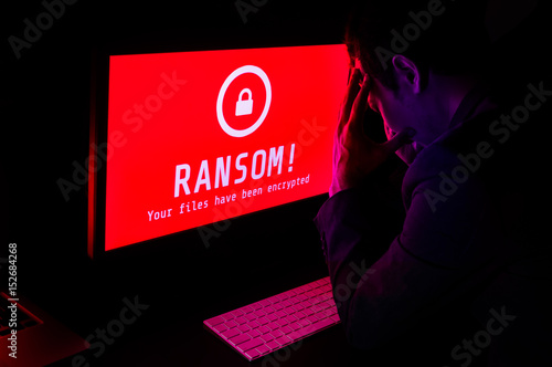 Computer screen with ransomware attack file encrypted alerts in red and a man in suit get stress in a dark room, ideal for online security failure and digital crime, long exposure selective focus photo