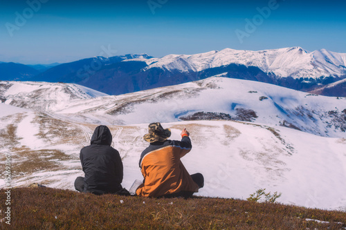 Two hikers sit on a hill and enjoy the mountain valley