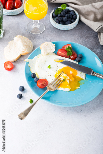 Fried egg on blue plate, tomatoes, blueberries and orange juice. Healthy breakfast concept with copy space.