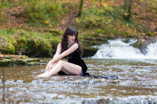 Young girl in a black dress posing on the edge of a waterfall