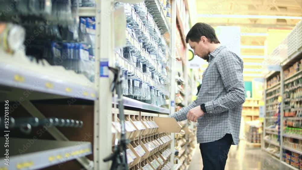 Shop with a tools department. Shelf with nails and fasteners and male customer. Man chooses self-tapping screws that he needs. Shop with a tools department. Shelf with nails and fasteners and male customer. Man chooses self-tapping screws that he needs.