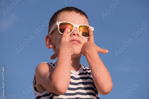 happy little kid wearing sunglasses and striped shirt on blue sky background