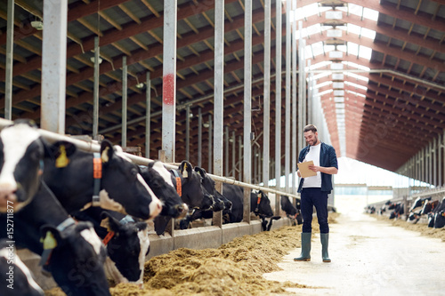 farmer with clipboard and cows in cowshed on farm