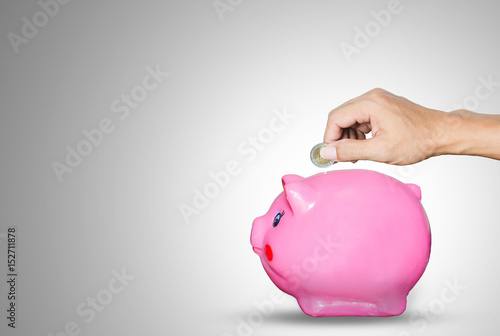 hands holding a coin put on piggy bank saving on gray background for saving money concept.