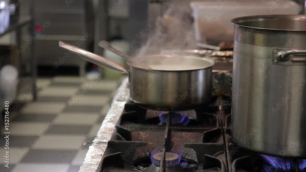 The kitchen cook removes the pan with a handle with a gas stove. The hand takes the bowler. On the working surface, boiling water in the saucepan for cooking soup. In the dining room, the staff The kitchen cook removes the pan with a handle with a gas stove. The hand takes the bowler. On the working surface, boiling water in the saucepan for cooking soup. In the dining room, the staff
