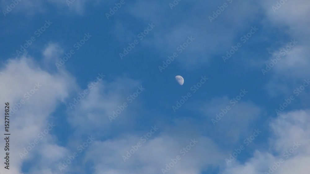 White moon by daylight. On blue sky among moving clouds, which hide it at the end. Early evening, spring. White moon by daylight. On blue sky among moving clouds, which hide it at the end. Early evening, spring.