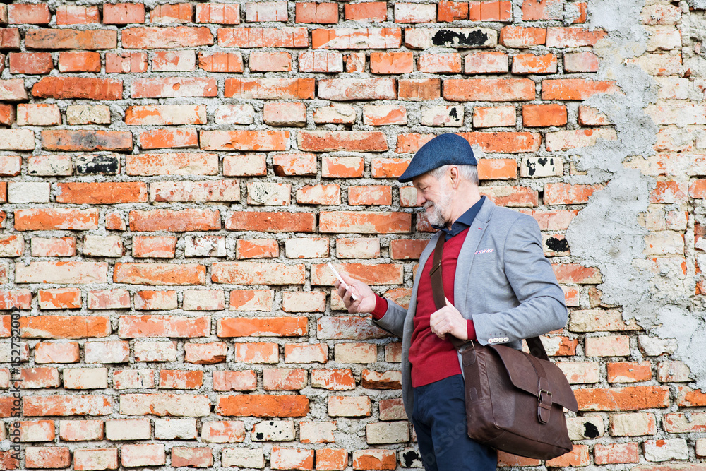 Senior man with smartphone against brick wall, texting. Senior man with smartphone against brick wall, texting.