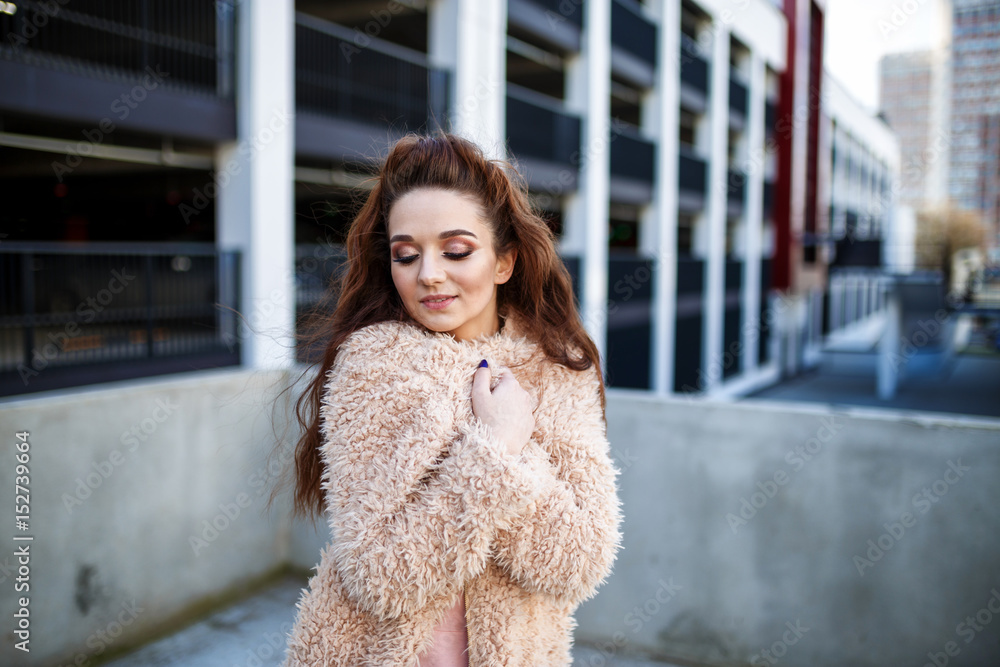 young beautiful happy girl in a coat posing at the street