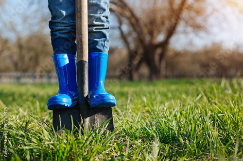 Close up of childs feet in rubber boots on shovel