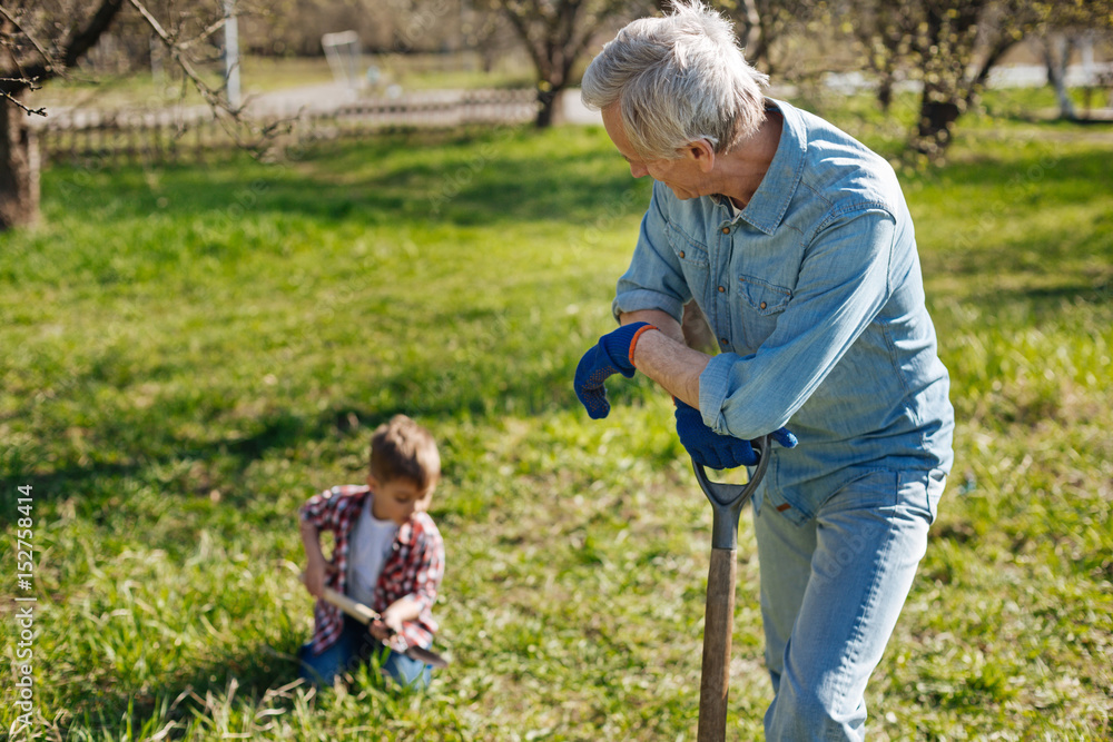 Senior man watching his grandson digging into soil Senior man watching his grandson digging into soil