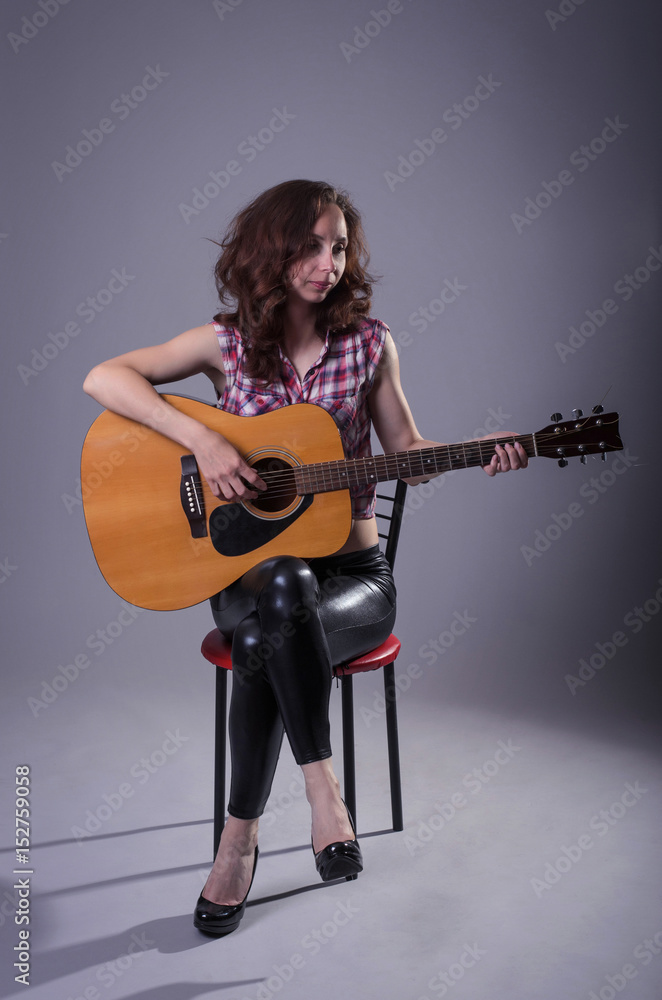 Young woman plays on an acoustic guitar, isolated on a gray background. Young woman plays on an acoustic guitar, isolated on a gray background.