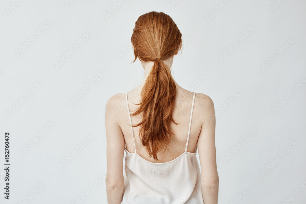Portrait of young pretty girl with foxy hair posing back to camera over white wall Portrait of young pretty girl with foxy hair posing back to camera over white wall