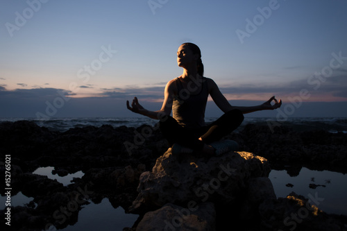 Yogi girl in lotus pose on the rocks near the sea at night