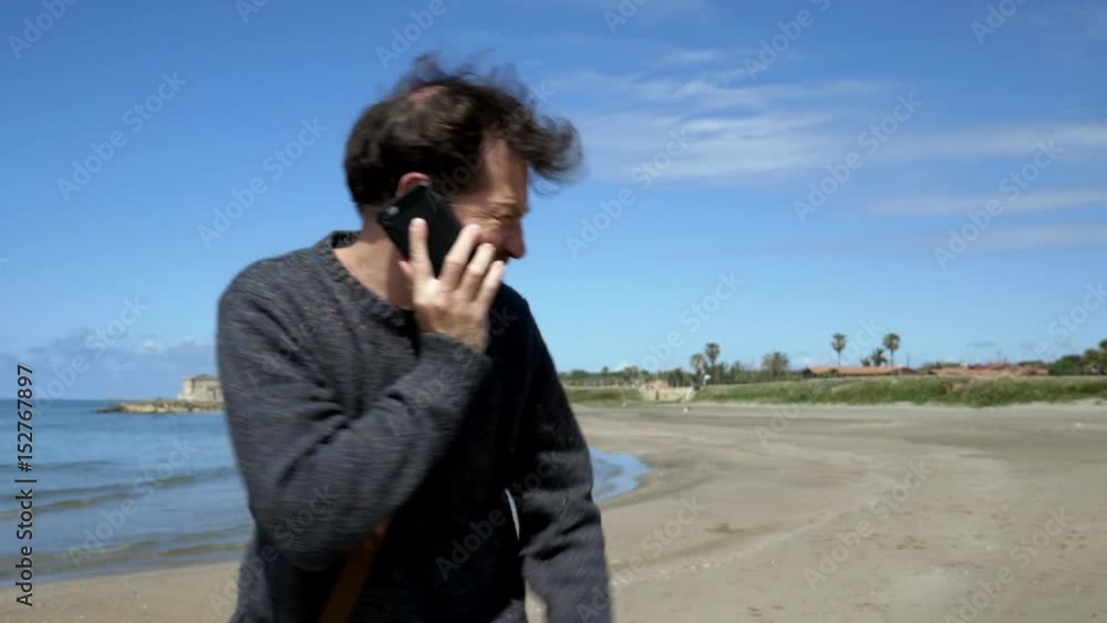 Happy man laughing talking on the phone walking on beach medium shot Happy man laughing talking on the phone walking on beach medium shot