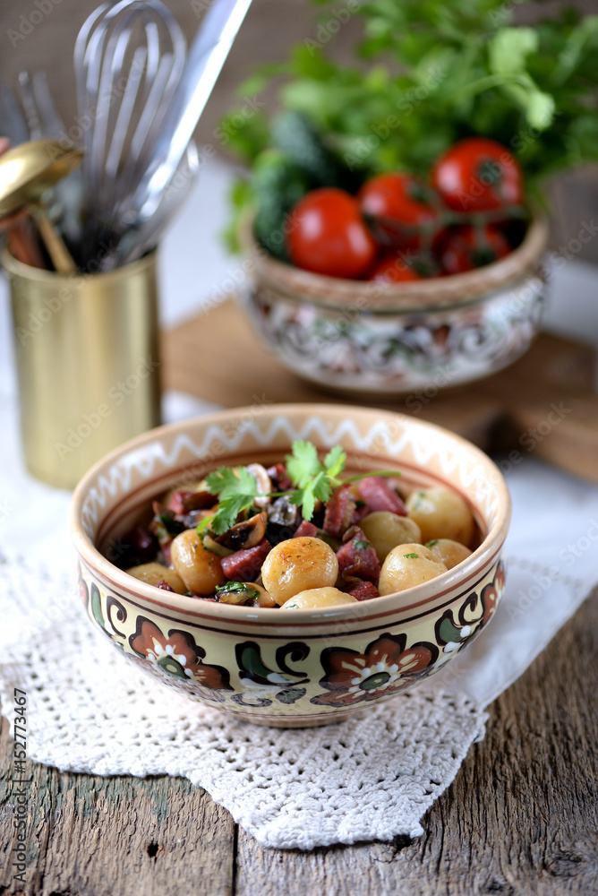 Small whole potato fried with sausage, mushrooms and onions on an old wooden background. Rustic style. Small whole potato fried with sausage, mushrooms and onions on an old wooden background. Rustic style.