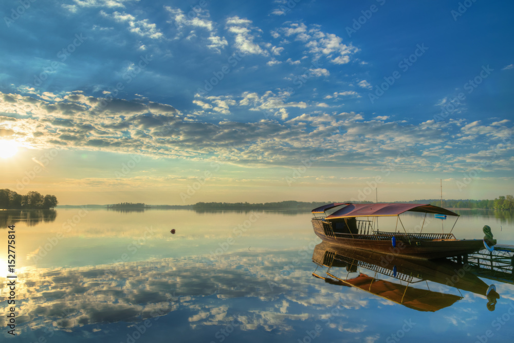 Sun rises over beautiful lake. Clouds are reflected in the water. HDR image.
