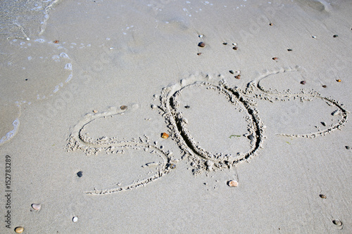 SOS - word drawn on the sand beach with the soft wave.