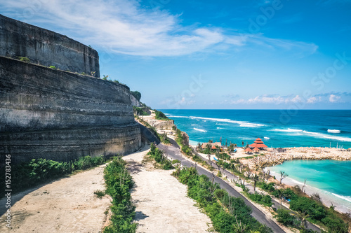 Scenic landscape of high cliff on tropical white sand beach in Bali island. Indonesia tropical nature outdoor landscape with scenic sea water and white foam waves from above