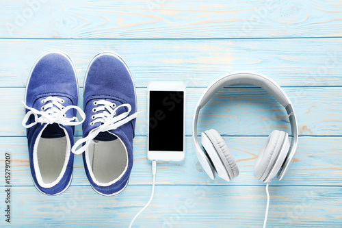 Sport shoes with smartphone and headphones on blue wooden table