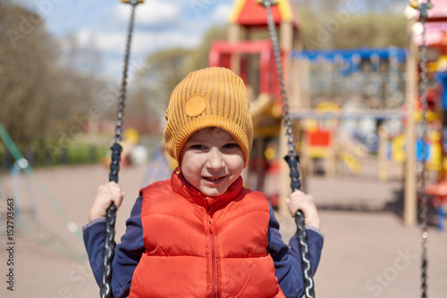 Cute smiling boy is swinging on children’s playground.