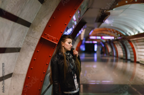 Beautiful young woman in black leather jacket posing against the backdrop of the red iron beams. Held by the collar. The urban style.