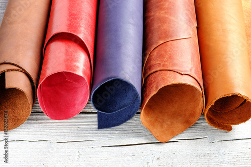 Brightly colored leather in rolls on the white wooden background. Leather craft.