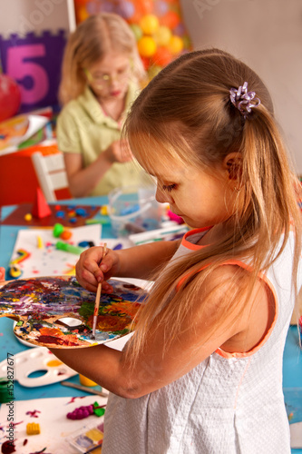 Small student girl painting in art school class. Child drawing by paints on table. Portrait of kids in kindergarten. Craft drawing education develops creative abilities of children. Children learn to
