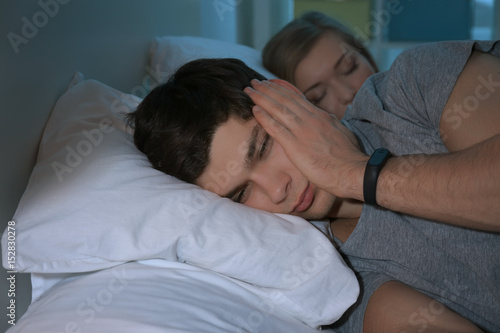 Young man with sleep disorder lying on bed at home
