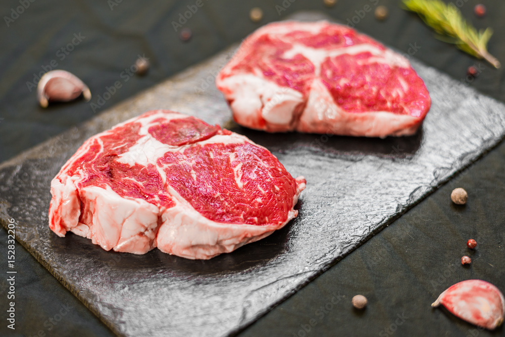 Rib eye beef cow steak meat with spices and herbs against black background