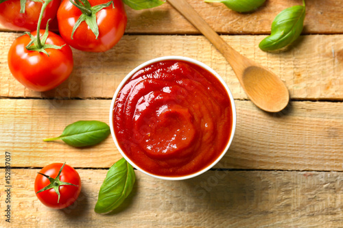 Delicious ketchup with basil and tomatoes on wooden background