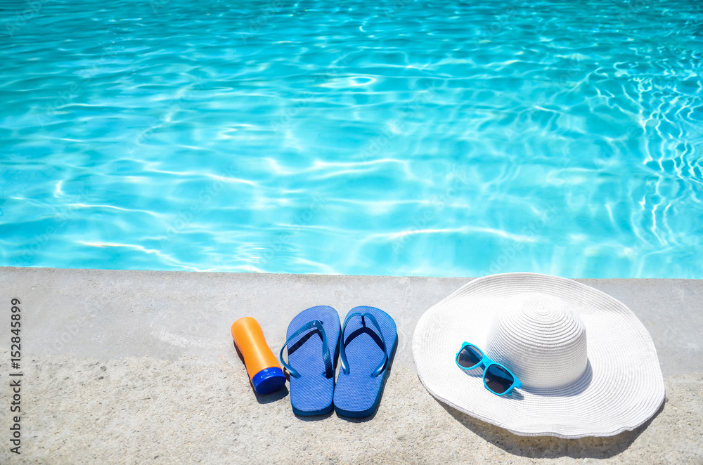 Summer background with hat, sunscreen, flip flops and sunglasses near the pool
