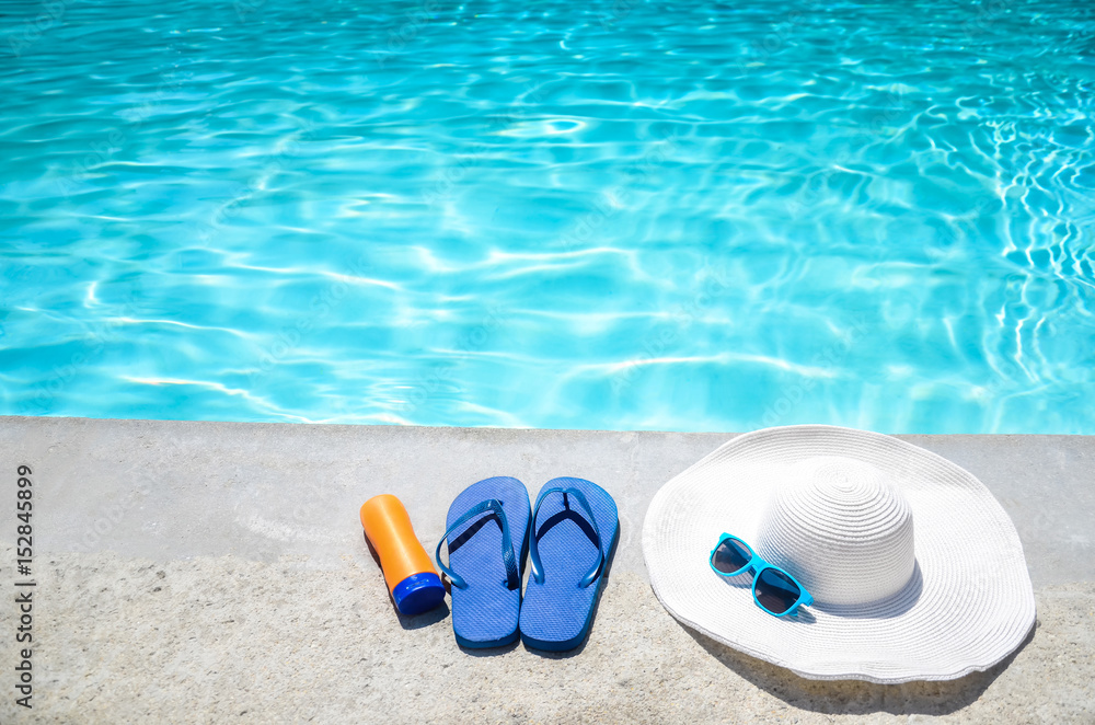 Summer background with hat, sunscreen, flip flops and sunglasses near the pool Summer background with hat, sunscreen, flip flops and sunglasses near the pool