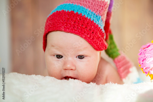 A newborn baby with a red hat on his head lies on his stomach. Portrait