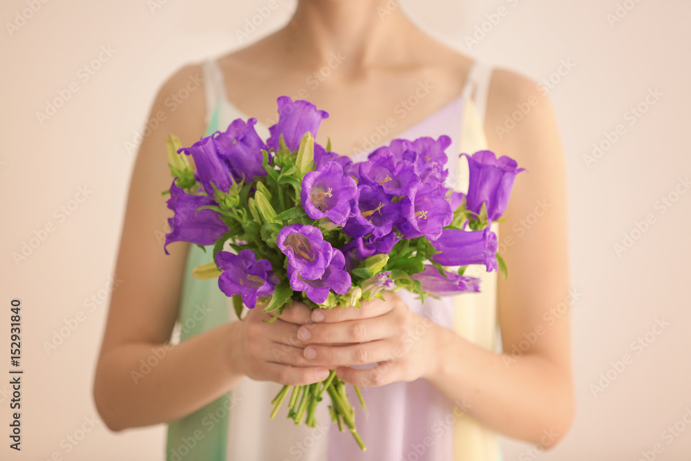 Woman holding beautiful bouquet of purple bellflowers on light background