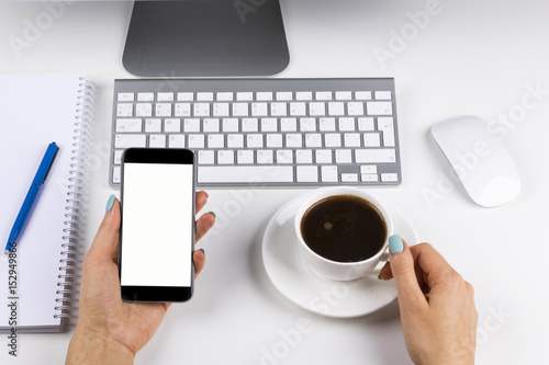 Woman hands holding the phone with isolated screen and cup of coffee. Business workplace with keyboard and business objects