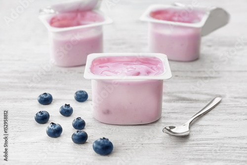 Plastic cup with yogurt and blueberries on wooden table
