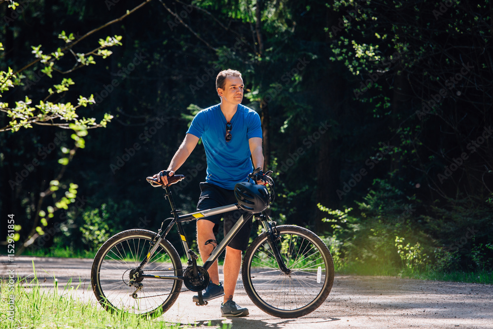 Young man in blue shirt standing with bicycle on the forest road. Healthy lifestyle concept. Sports guy with bike. Young man in blue shirt standing with bicycle on the forest road. Healthy lifestyle concept. Sports guy with bike.