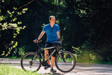 Young man in blue shirt standing with bicycle on the forest road. Healthy lifestyle concept. Sports guy with bike.