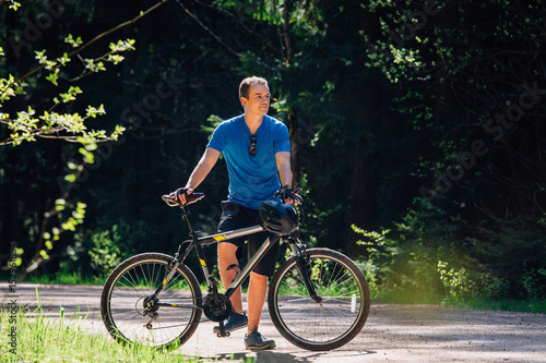 Young man in blue shirt standing with bicycle on the forest road. Healthy lifestyle concept. Sports guy with bike.